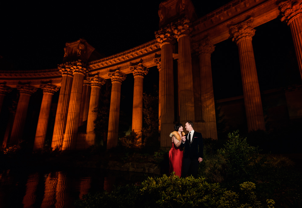 Natalie and Crockett looking at each other under the red columns during the Epic Couple's Session at Palace of Fine Arts in San Francisco | Lazzat Photography